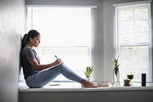 Woman sitting in widow seat writing in notebook.
