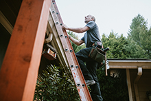 A contractor climbing a ladder to a roof.