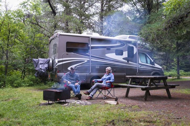 Couple sitting outside of the RV near their camp.