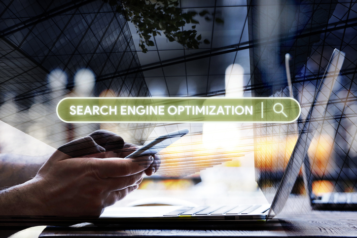 A person using their smartphone in the background with the phrase, search engine optimization, displayed in the foreground.