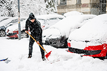 Man shoveling snow in front of cars.