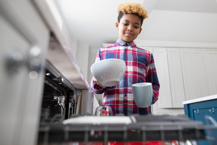 A boy putting dishes in the dishwasher.