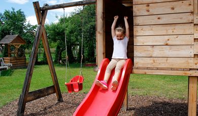 A girl sliding down a slide in the backyard. 