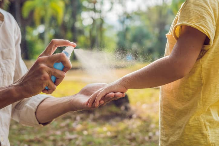 Mother spraying bug spray on her child.