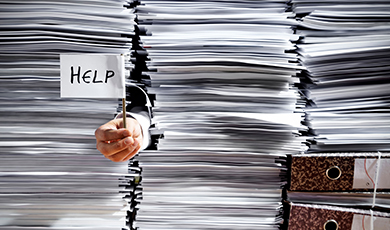 A hand holds a white flag labeled 'help.' The person holding the flag is buried beneath a large stack of papers. 