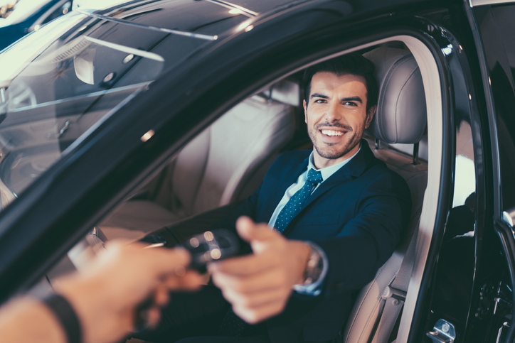 A man in the driver seat receiving keys to his rental car.