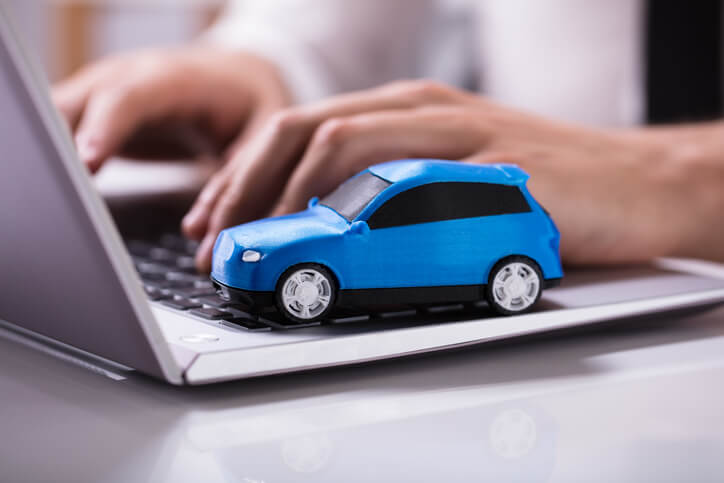 A person typing on their laptop while a toy SUV sits on the side of the keyboard.