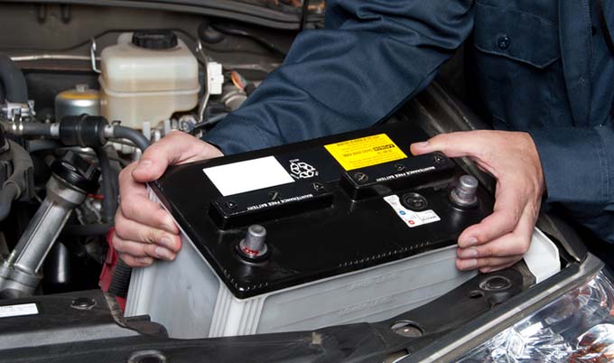A mechanic pulling a car battery from the hood of a vehicle.