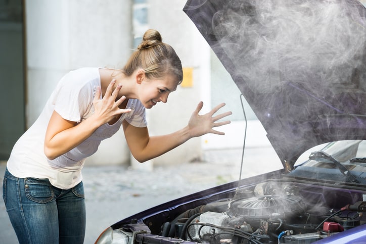 Woman with hands up in the air frustrated while looking at her smoking engine.