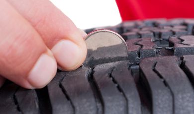 A person using a coin checks the depth of a tire tread. 