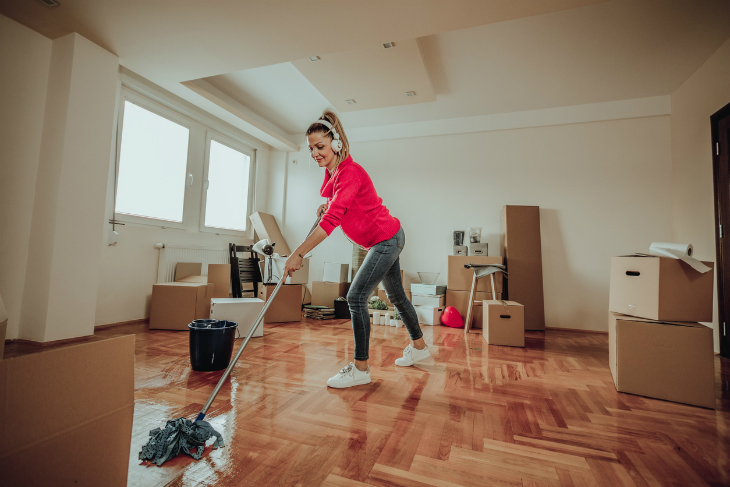 A woman with headphones on mopping hardwood floors.
