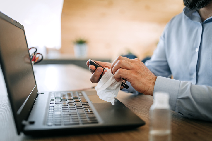 Man cleaning his smartphone and laptop with a sanitary wipe.