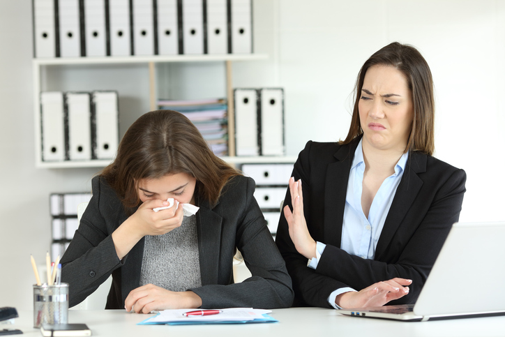 Co-worker shielding another co-worker's sneeze away from her direction.