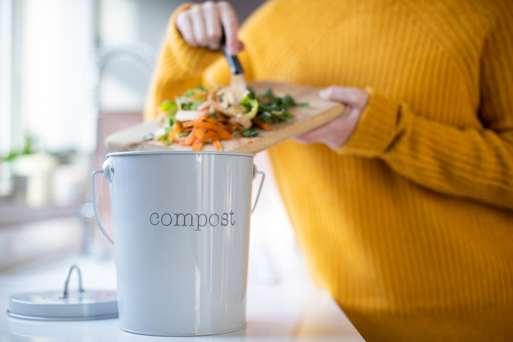 Woman scrapping leftover vegetables into a compost bin