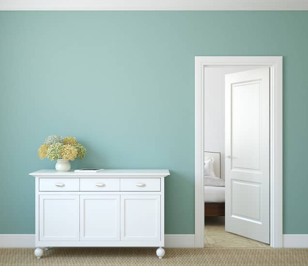 White dresser next to an open door leading to a bed room.
