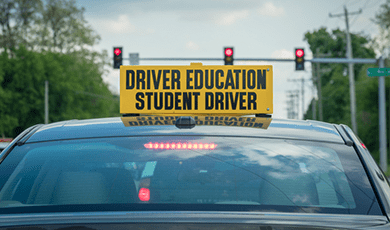 Car with Driver Education Student driver sign on the roof at a red light.