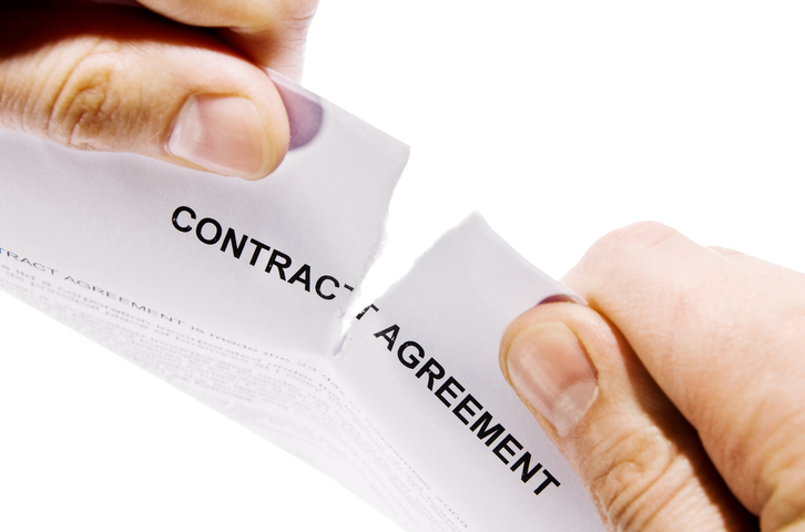 Hands ripping a document labeled contract agrement in half.