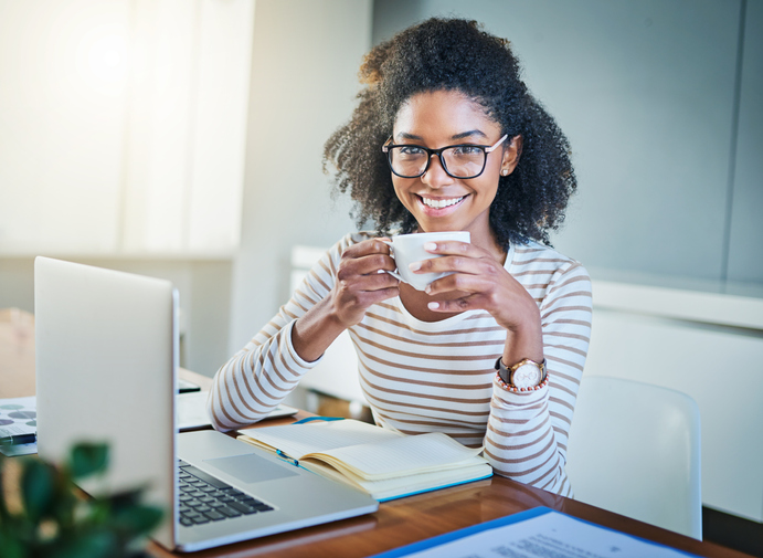 A woman posing with her cup of tea and work computer open.