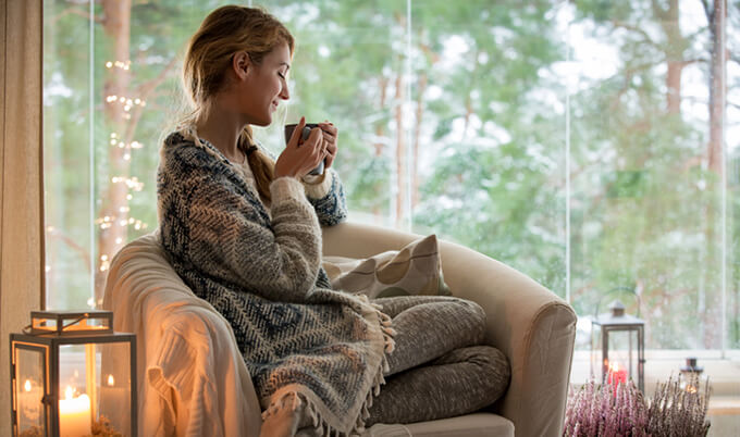 A woman sitting in her couch smelling her cup of tea.
