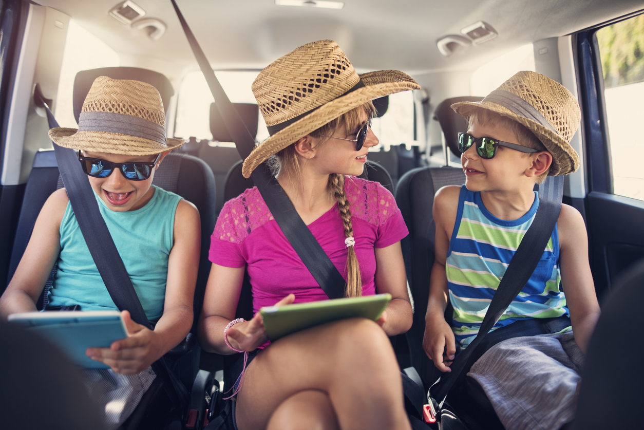 Three kids in the car backseat on their tablets.