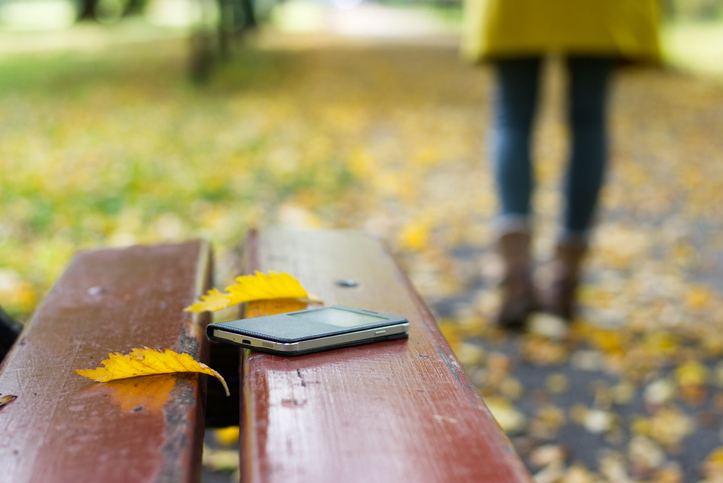 A person walking away from their smartphone left on a park bench.