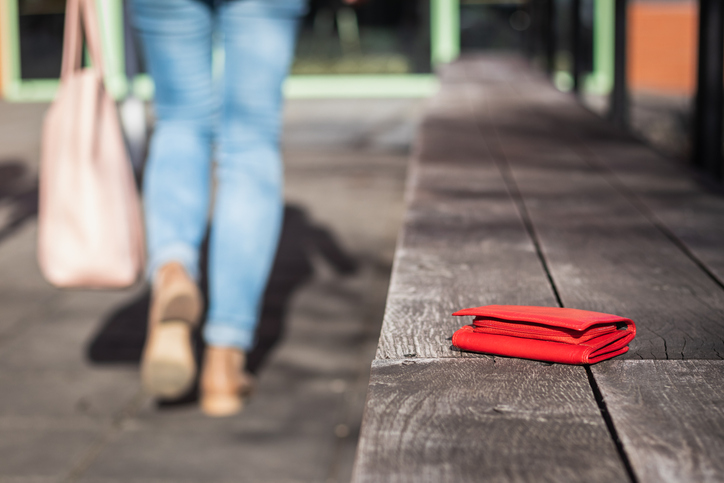 A person walking away from their wallet left on a outdoor wooden bench.