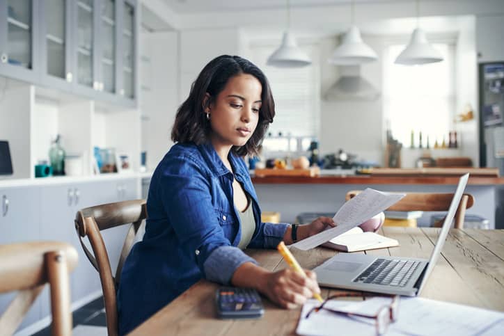 Woman taking notes at her work desk in front of a computer.