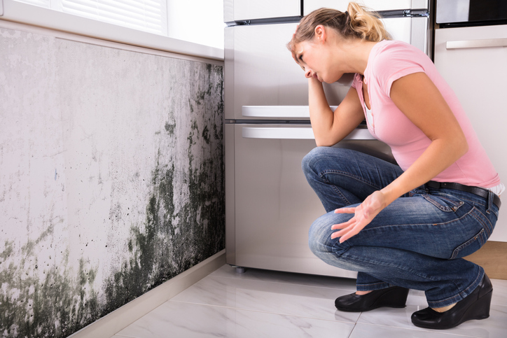 A woman looking at mold damage on the wall. 