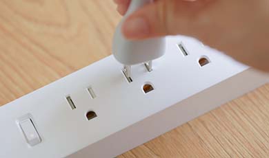 Person's hand plugging cord into a surge protector outlets.