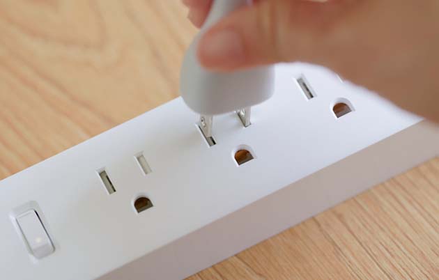 Person's hand plugging cord into a surge protector outlets.