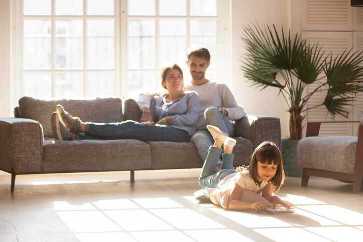 Couple sitting on the couch watching their daughter on the floor playing.