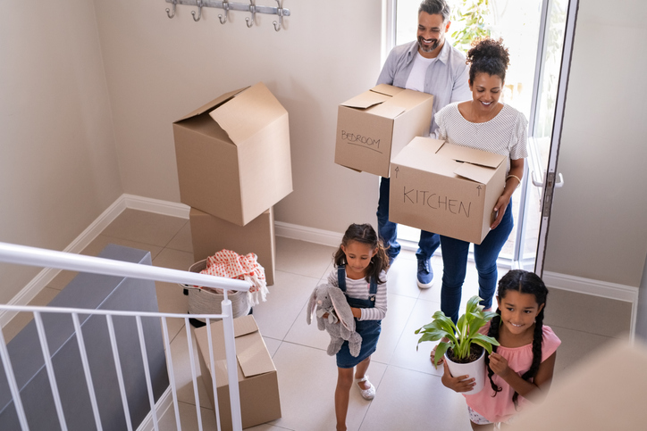 Mom and dad with two daughters holding boxes well walking into their new home.