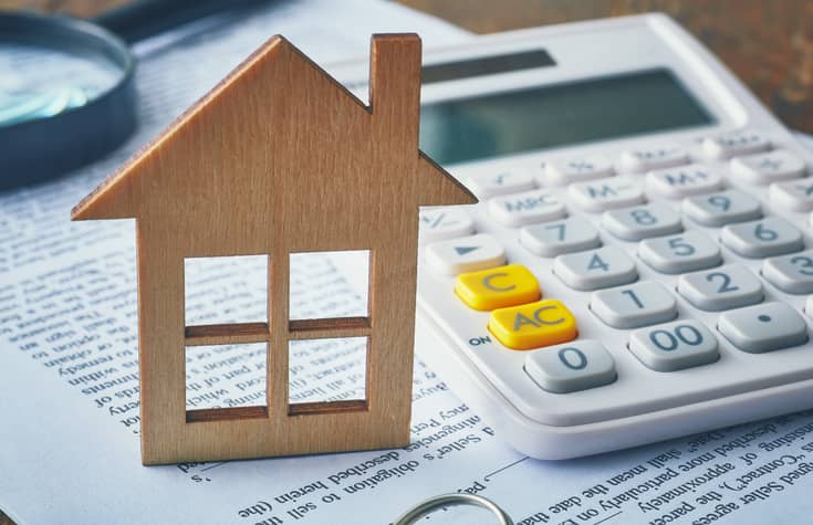 Small wooden cutout house next to a calculator.