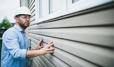 Contractor with a hard hat inspecting the siding of a home.