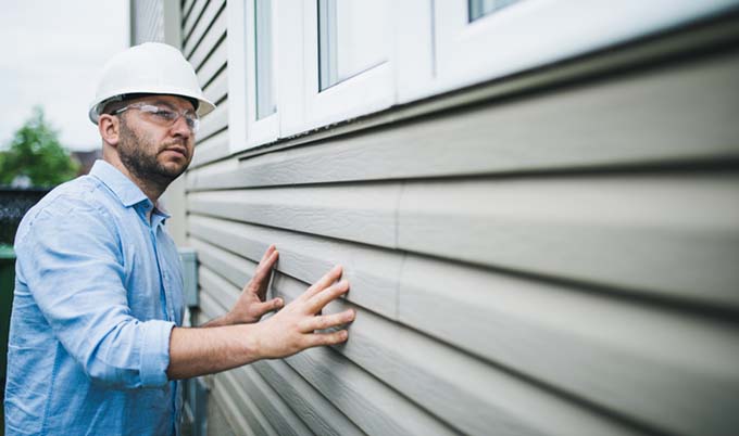 Contractor with a hard hat inspecting the siding of a home.