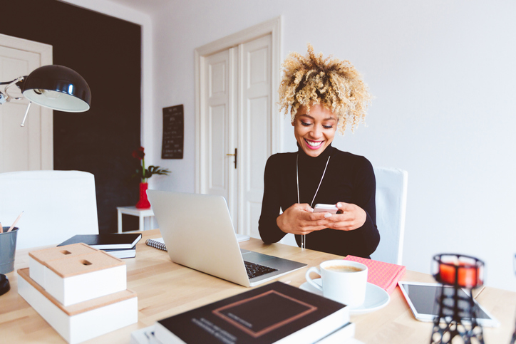 A woman smiling while looking at her smartphone.