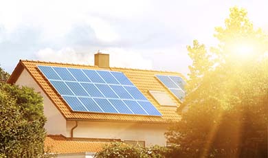 View of solar panels on the roof of a house with the sun glare in the distance.