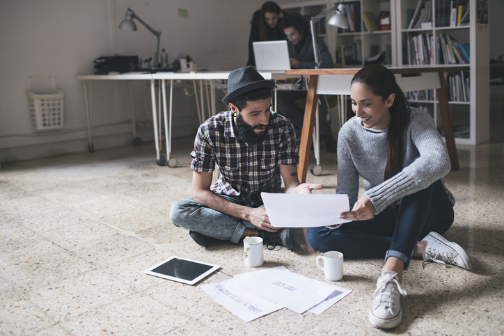 Man and woman sitting on the floor looking at paperwork.