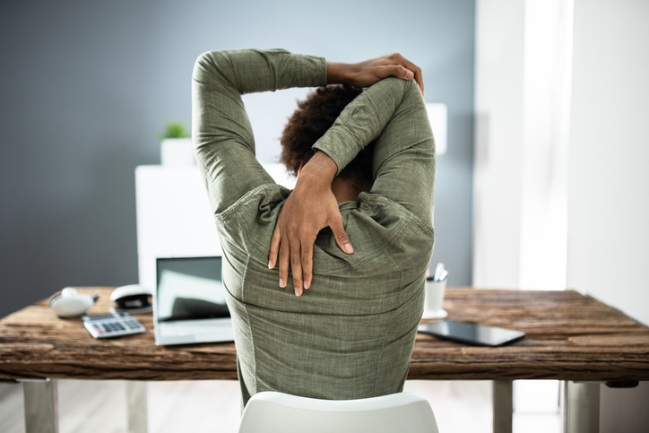 Person sitting at a work desk stretching their shoulder.
