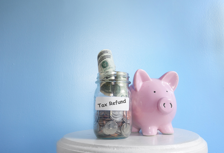 A jar of cash and change labeled tax refund near a piggy bank.