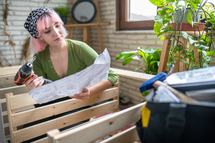 Woman holding a handheld drill while viewing instructions for a wooden box.