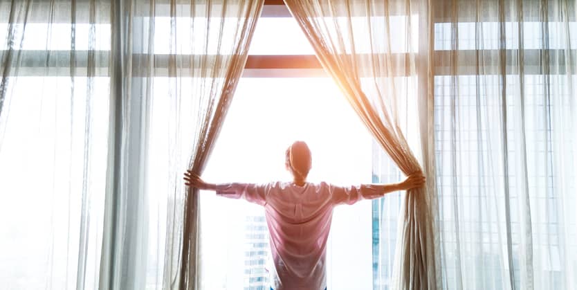 Woman opening her window curtains for sunlight.
