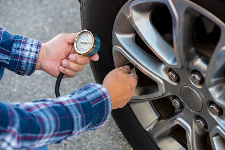 A man checking the air pressure in a car's tire.