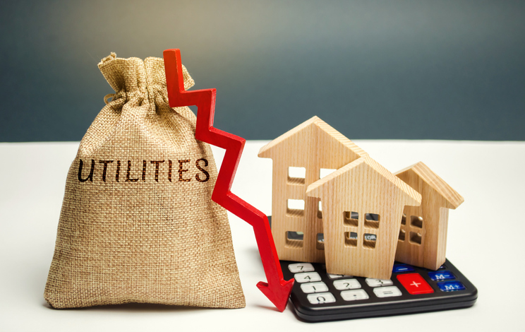 Money bag labeled Utilities positioned next wooden cut out houses on top of a calculator.