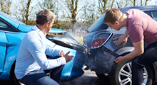 Two men bent over looking at a car accident. 