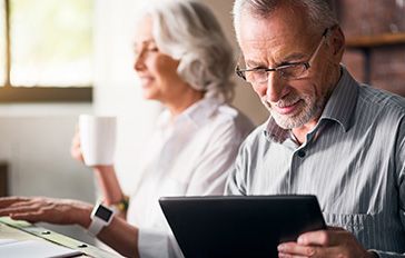 Older couple looking at a tablet and computer. 